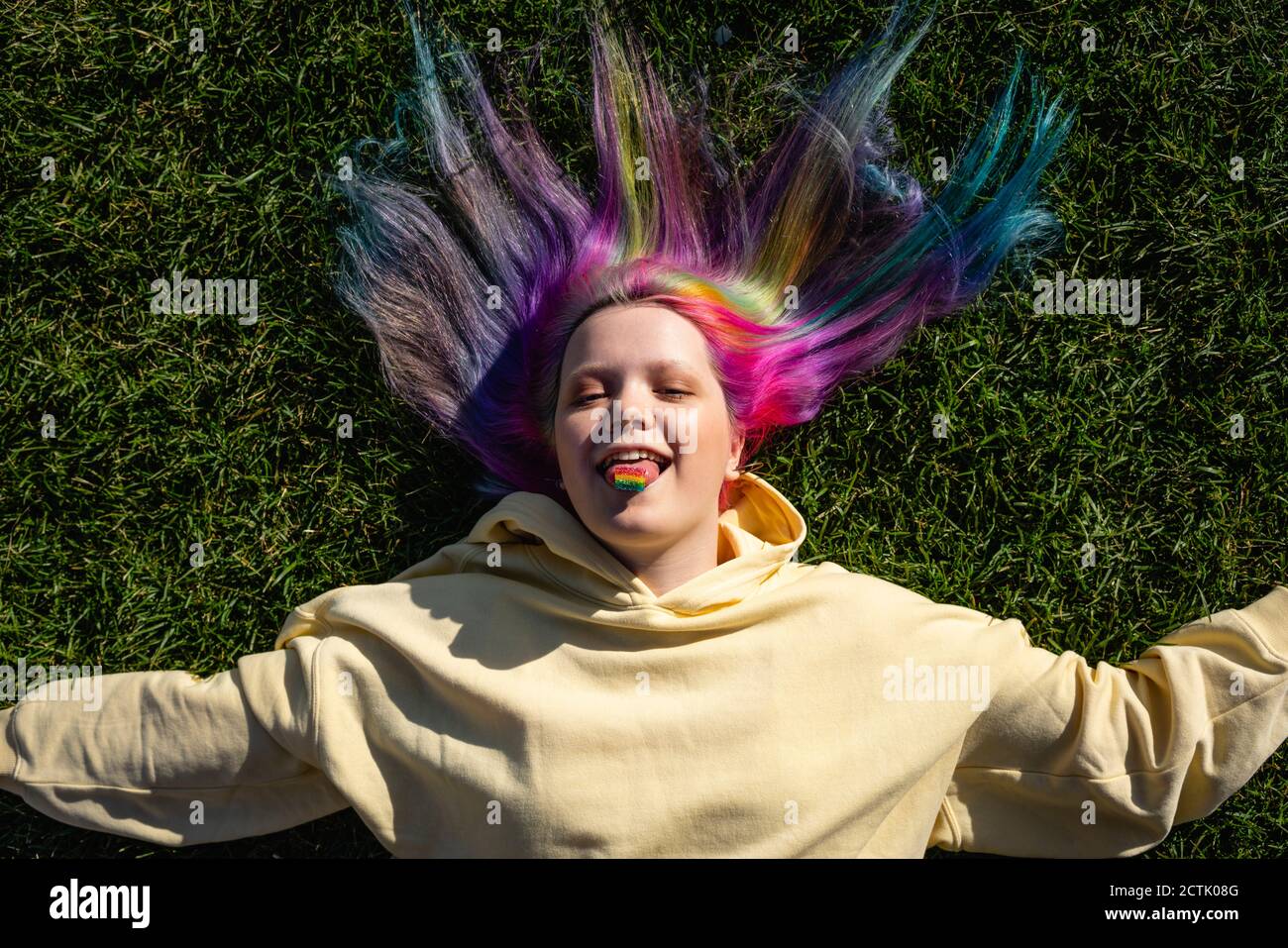 Retrato de una joven con cabello teñido y caramelo de arco iris tumbado en la pradera Foto de stock