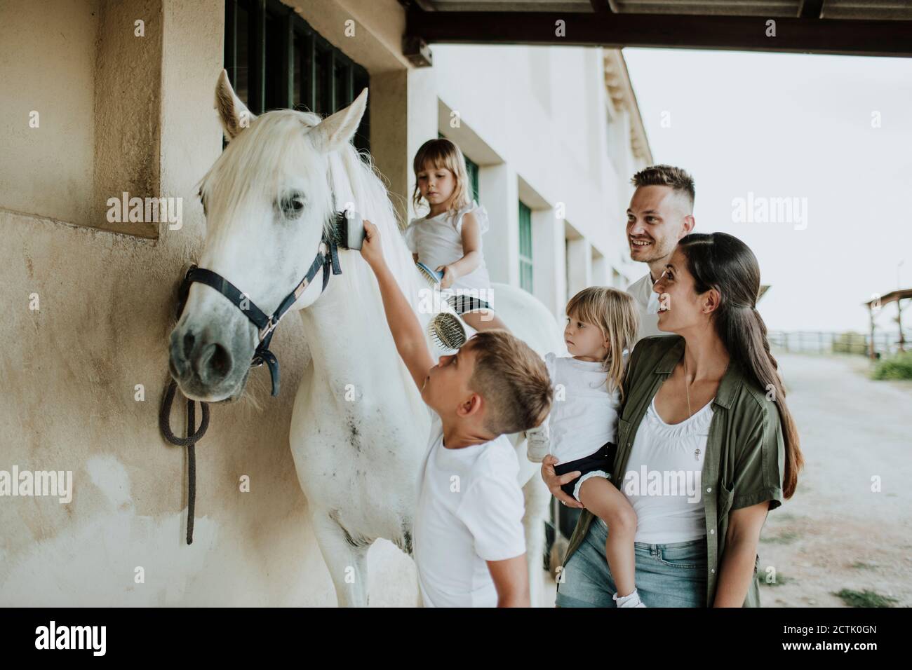 Los padres miran a los niños cepillándose el caballo mientras están de pie al aire libre Foto de stock