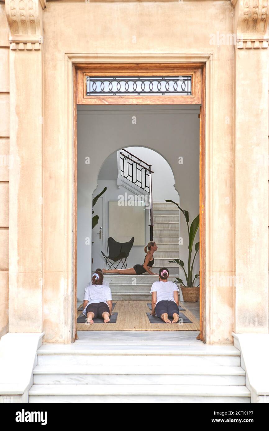 Instructor de yoga con mujeres practicando la postura de cobra en el estudio visto a través de la entrada Foto de stock