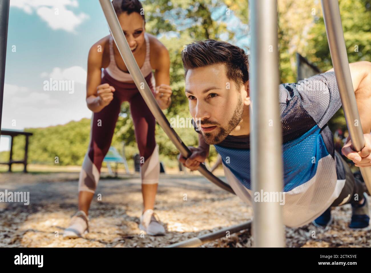 Mujer apoyando al hombre haciendo ejercicios de prensa en una pista de fitness Foto de stock