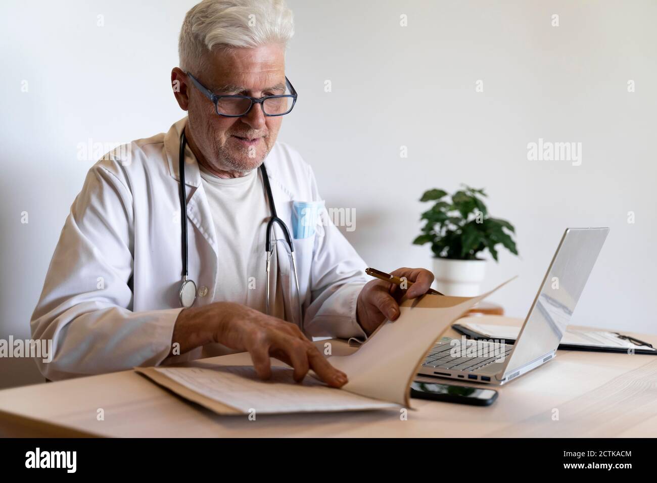 Médico de cabecera mirando el expediente médico mientras está sentado en la  clínica Fotografía de stock - Alamy