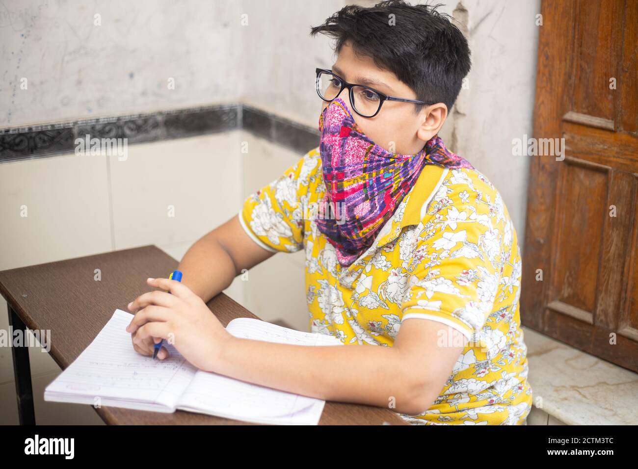 Estudiante de niño indio que estudia en el salón de clases usando máscara manteniendo el distanciamiento social mira la cámara, la escuela reabre durante la pandemia de covid19 Foto de stock