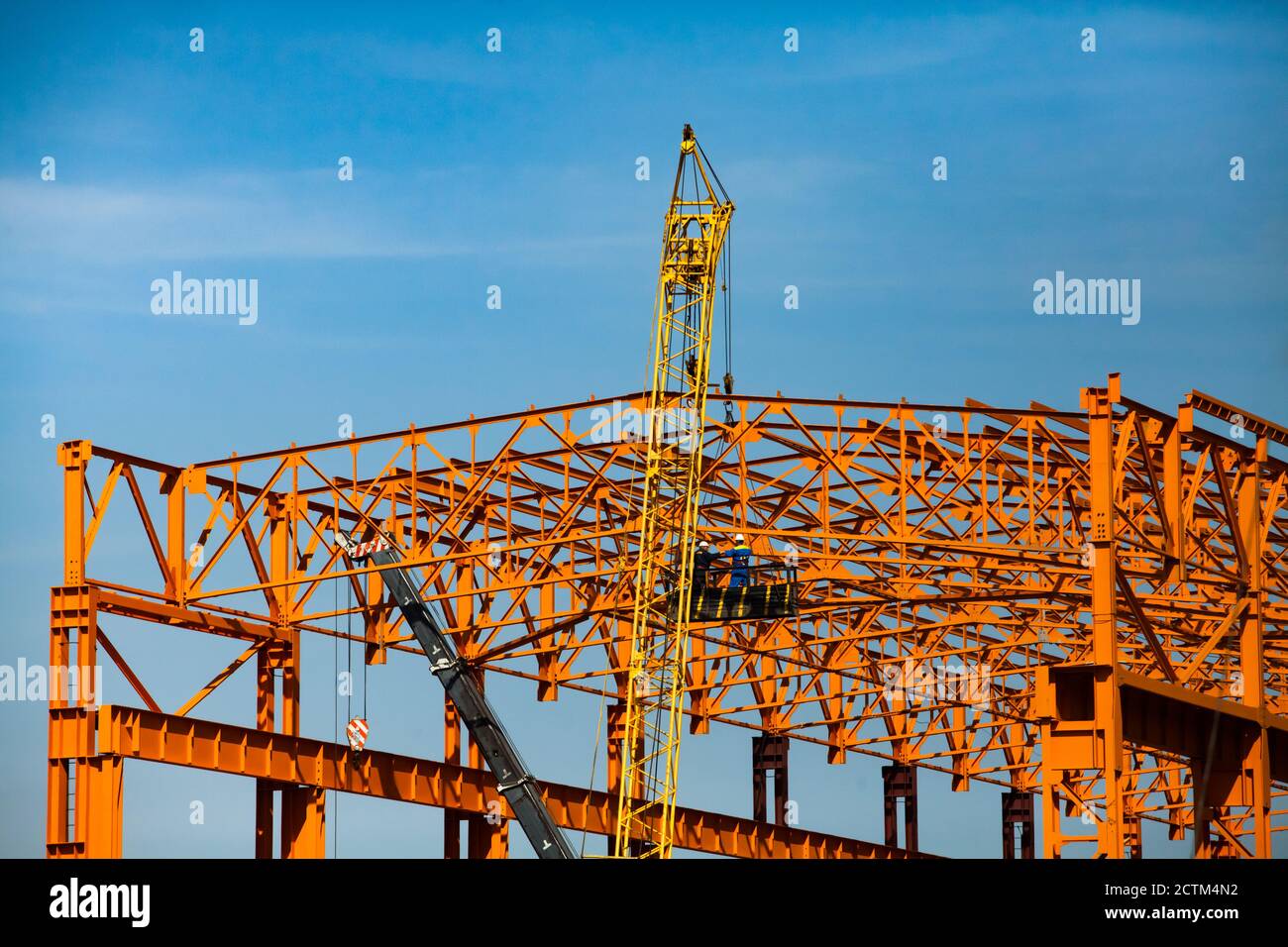 Construcción de una nueva estructura de construcción de acero naranja. Dos trabajadores en cuna suspendida. Trabajos inseguros para el montaje de construcciones metálicas Foto de stock