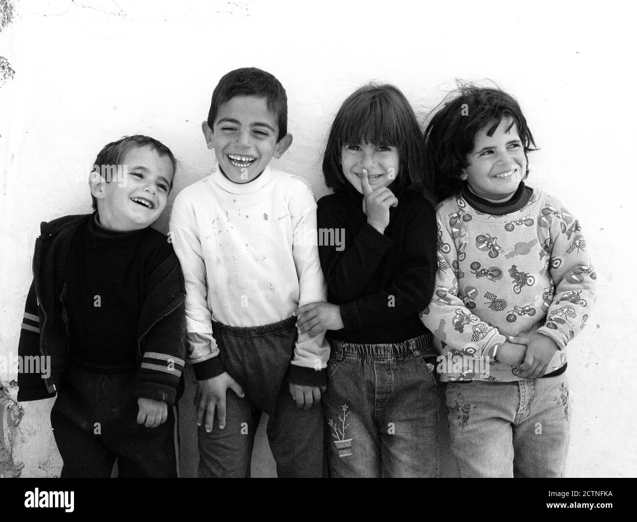 4 niños contra una pared blanca se ríen cara a cara con complicidad Foto de stock