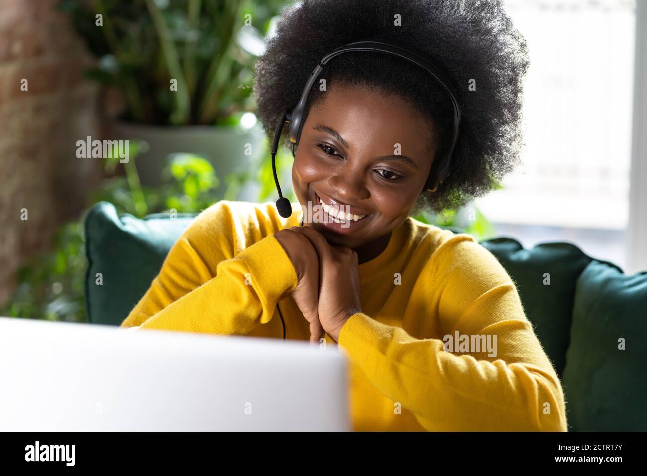 Mujer milenaria afroamericana sonriente llevar auriculares hablar videollamada, utilizar el portátil, enseñar en línea, comunicarse a través de la aplicación zoom, ver seminario web Foto de stock