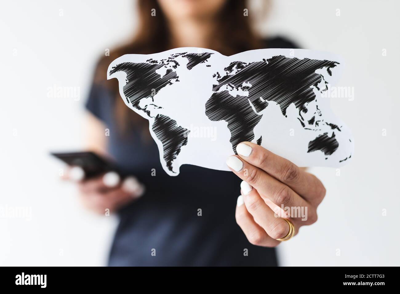 concepto de comercio mundial o viajes internacionales, mujer que sostiene el mapa del mundo hacia la cámara mientras navega algo en su smartphone filmado en shal Foto de stock