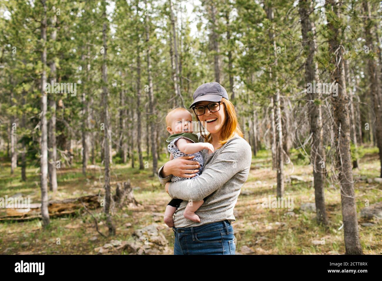 Retrato de una mujer sonriente sosteniendo a un bebé (6-11 meses) en el bosque, Wasatch Cache National Forest Foto de stock