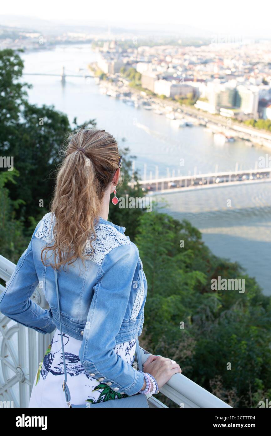 Mujer joven en chaqueta de vaquero preguntándose en panorama de la ciudad Foto de stock