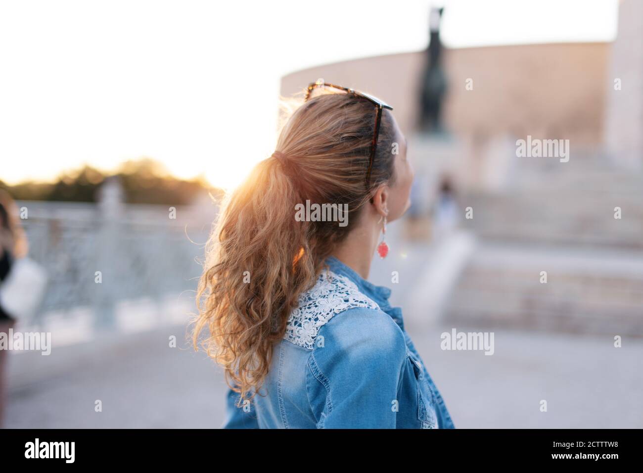 Mujer joven mirando hacia arriba monumento famoso lugar vista de atrás en puesta de sol Foto de stock