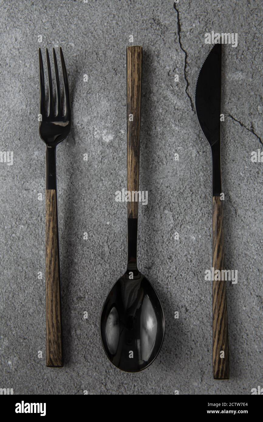 Cubiertos negros sobre fondo de hormigón gris. Cuchara, tenedor, cuchillo  con mangos de madera Fotografía de stock - Alamy