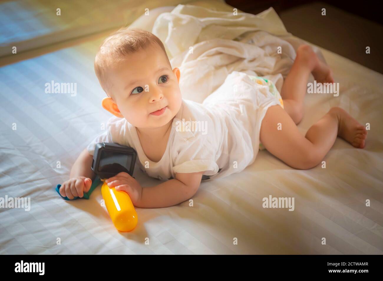 Un Bebe De 8 Meses Descansa Sobre Una Cama Blanca Una Nina Juega Con La Camara De Accion Y Mira A La Mama Fotografia De Stock Alamy