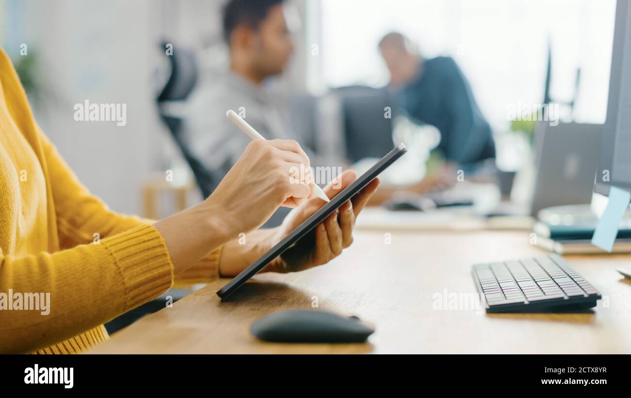 Mujer joven anónima sentada en su escritorio ella está dibujar, escribiendo y usando el lápiz con la computadora de la tableta digital. Céntrese en las manos con Pen. Oficina Bright Foto de stock