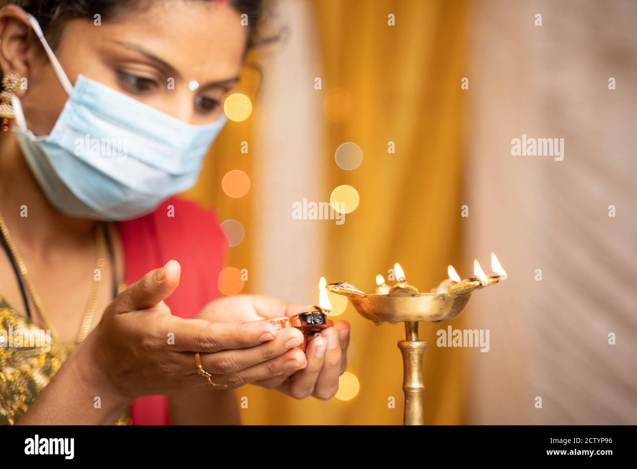 Enfoque selectivo en las manos, la mujer India en la linterna de iluminación de máscara médica o lámpara Diya durante el festival en casa - concepto de festival tradicional Foto de stock