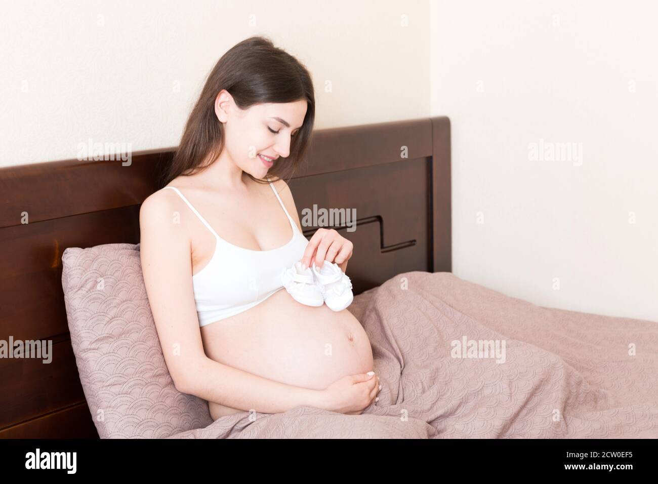 Mujer embarazada con pequeños zapatos de bebé sentada en la cama en casa  Fotografía de stock - Alamy
