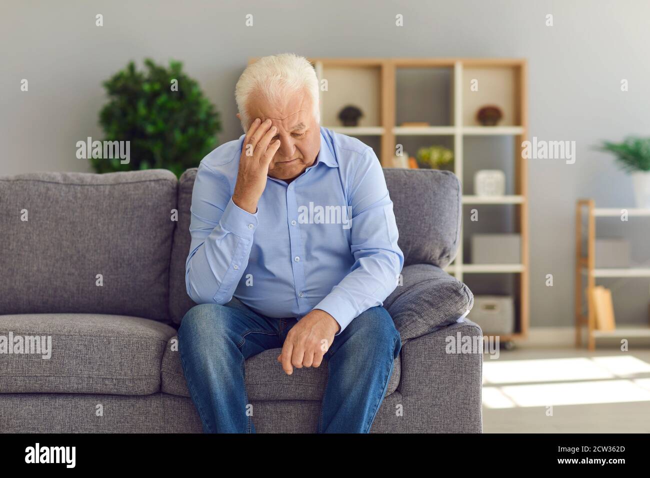 Deprimido anciano sentado en el sofá en casa sufriendo de soledad o dolor de cabeza malo Foto de stock