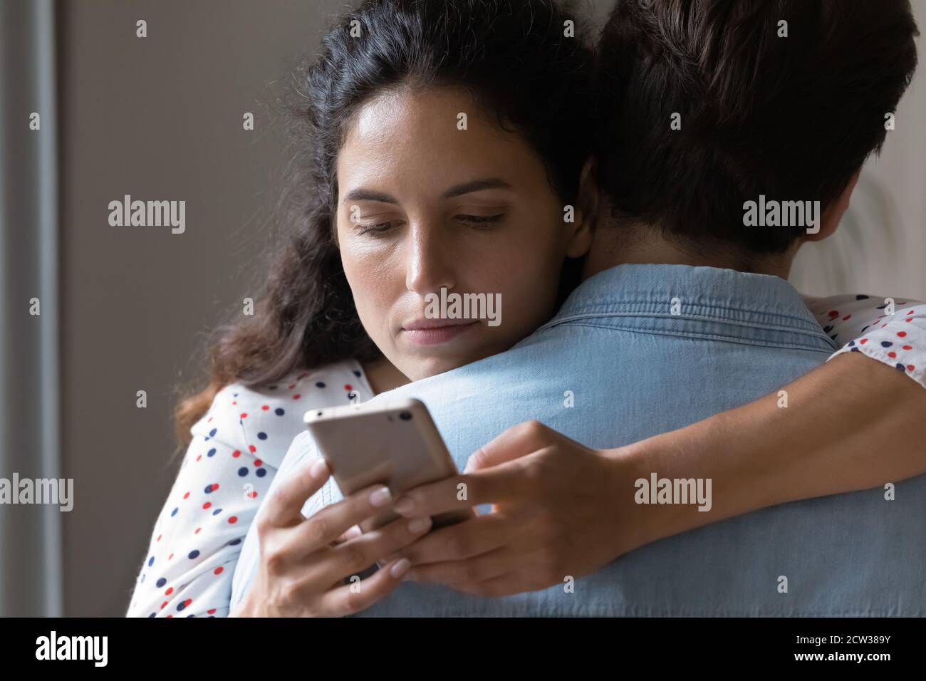 Mujer joven abrazo marido engaño en línea en el teléfono celular Foto de stock
