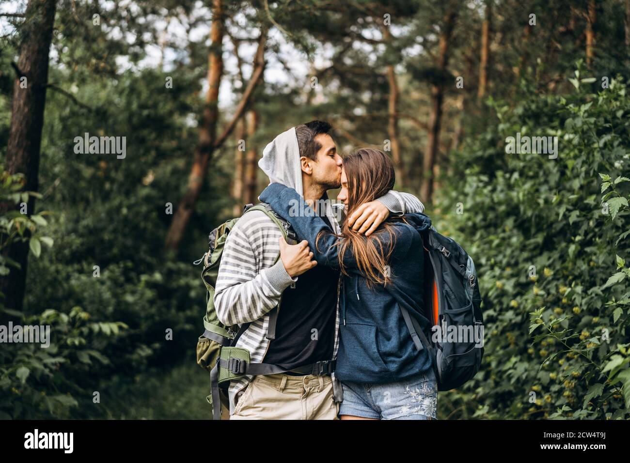Pareja joven con mochilas en la espalda sonriendo y caminando por el bosque, disfrutar del paseo. Foto de stock