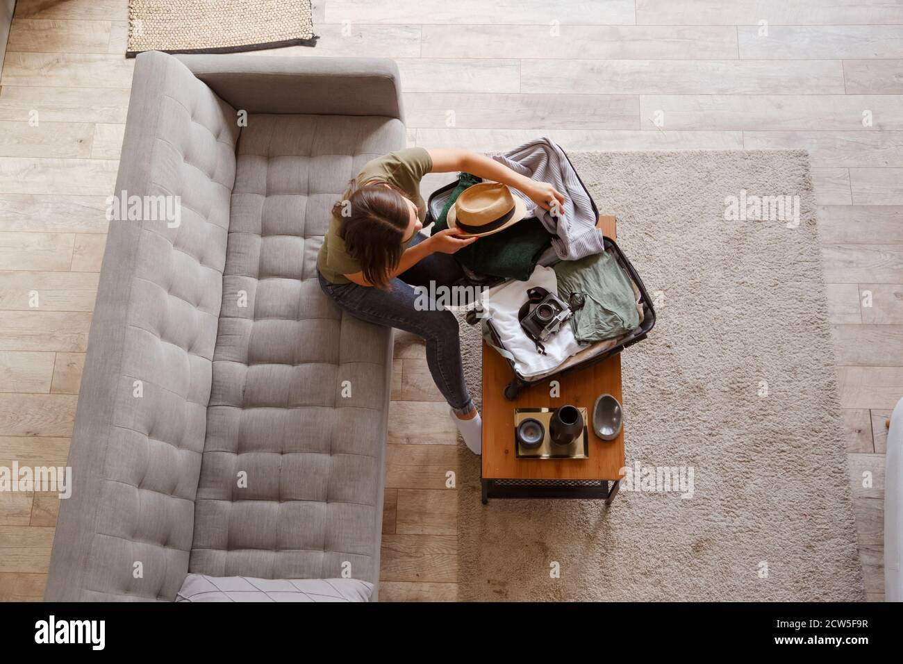 Preparación de la maleta para un viaje de vacaciones. Mujer joven revisando ropa y cosas en el equipaje en el sofá. Vista desde arriba Foto de stock