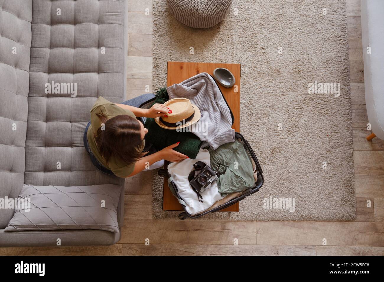 Preparación de la maleta para un viaje de vacaciones. Mujer joven revisando ropa y cosas en el equipaje en el sofá. Vista desde arriba Foto de stock