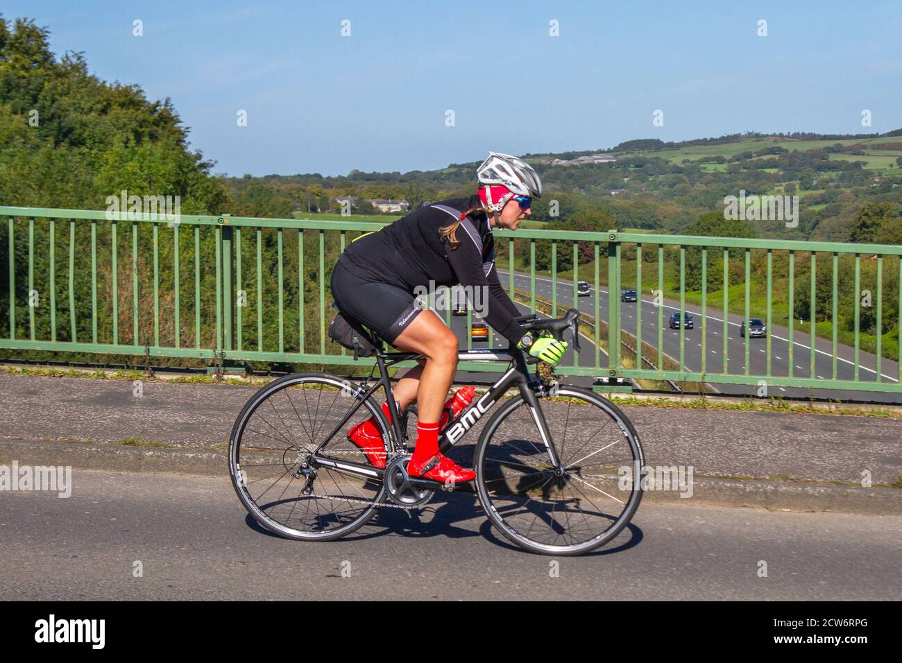 Mujer ciclista montar BMC deportes máquina bicicleta de carretera en el campo ruta cruzando el puente de la autopista en la zona rural de Lancashire, Reino Unido Foto de stock