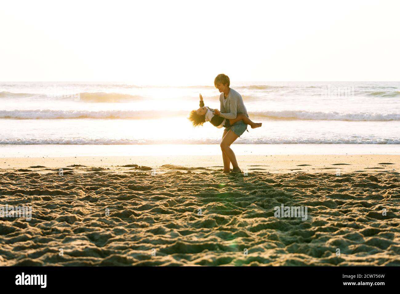 Niño girando en los brazos su madre muy feliz una puesta de sol en la playa Foto de stock