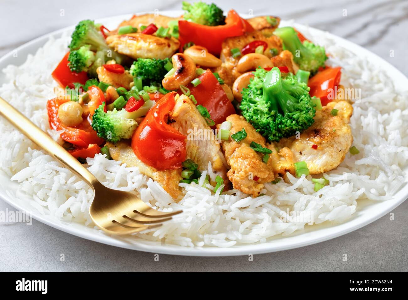Pollo de cajú asiático con verduras salteadas: Brócoli, pimiento, Chile rojo caliente y salsa de soja en un plato blanco con tenedor en un dorso de mármol blanco Fotografía de stock - Pollo de cajú asiático con verduras salteadas: Brócoli, pimiento, Chile rojo caliente y salsa de soja en un plato blanco con tenedor en un dorso de mármol blanco Fotografía de stock -