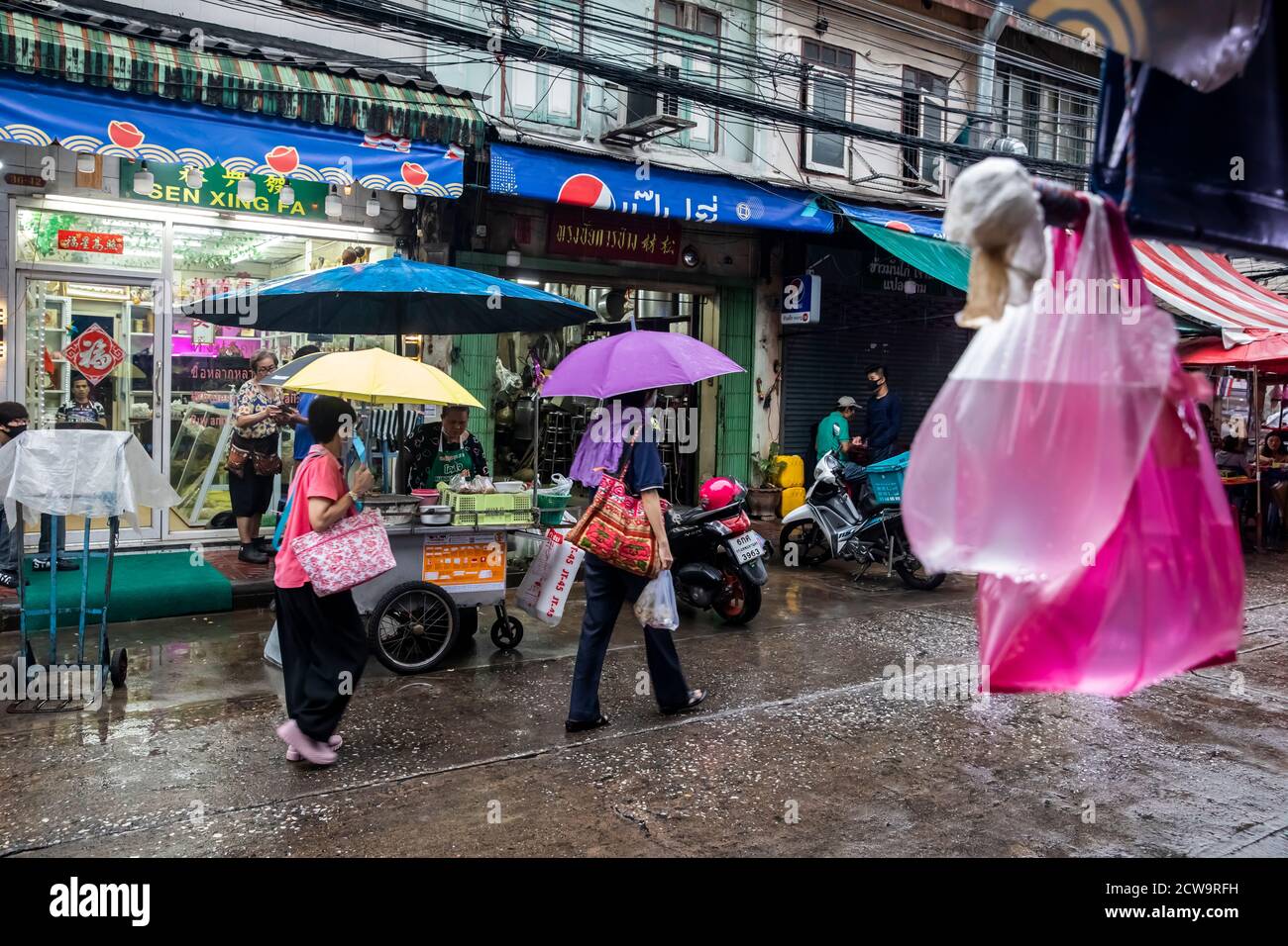Con dos bolsas de agua colgando de un toldo, peatones y motocicletas paran  en los vendedores para recoger comida callejera en el barrio chino de  Bangkok Fotografía de stock - Alamy