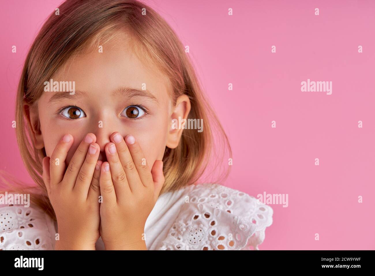 retrato de niña caucásica en shock, se sorprende por algo, mantener las manos en la boca, aislado fondo rosa Foto de stock