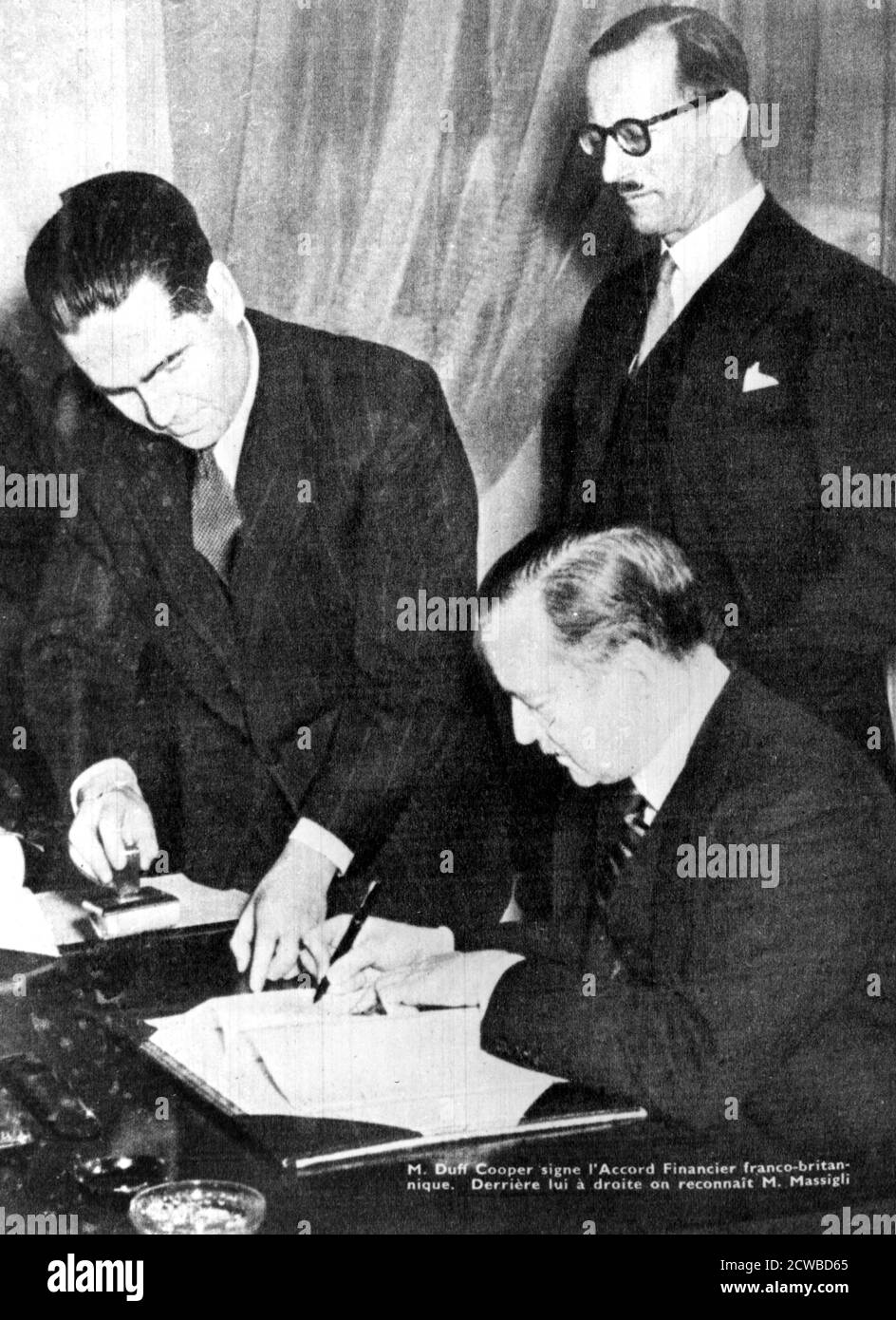 Firma del acuerdo financiero entre Gran Bretaña y el francés libre, Argel, 8 de febrero de 1944. Duff Cooper, enlace del Gobierno británico con el francés libre, firma el documento. Rene Massigli, el Comisario de Asuntos Exteriores de Francia libre, está detrás de él. El fotógrafo es desconocido. Foto de stock
