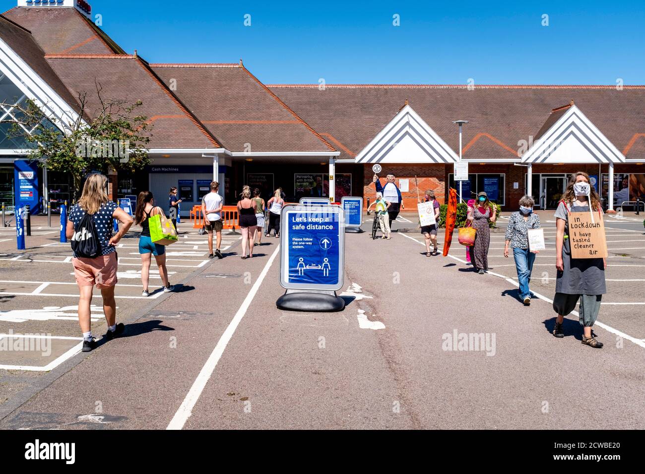 Manifestantes ambientales pasar por personas distanciamiento social en una cola de supermercado, Lewes, East Sussex, Reino Unido. Foto de stock