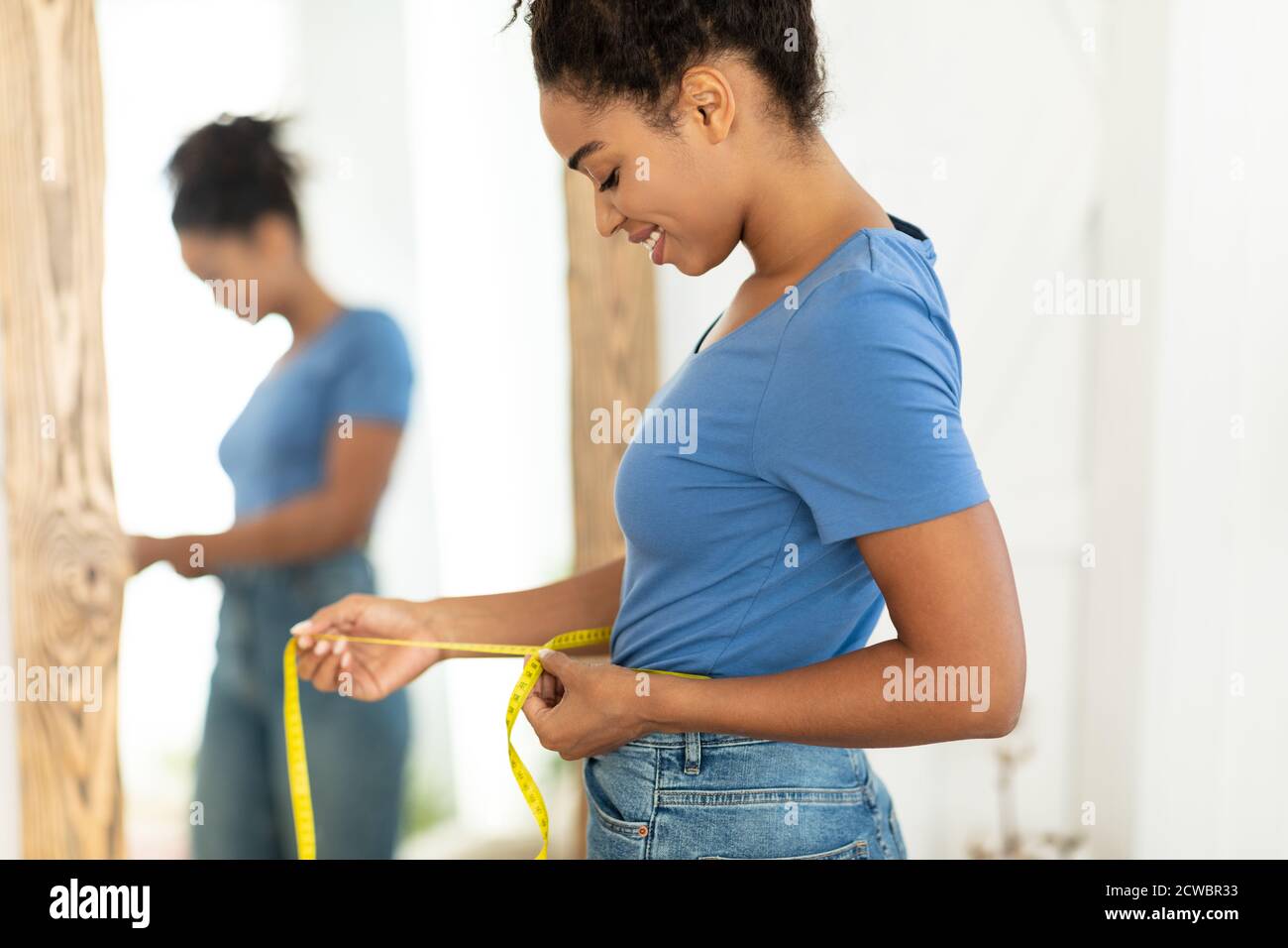 Mujer africana sonriente midiendo la cintura después de Slimming de pie en el hogar Foto de stock
