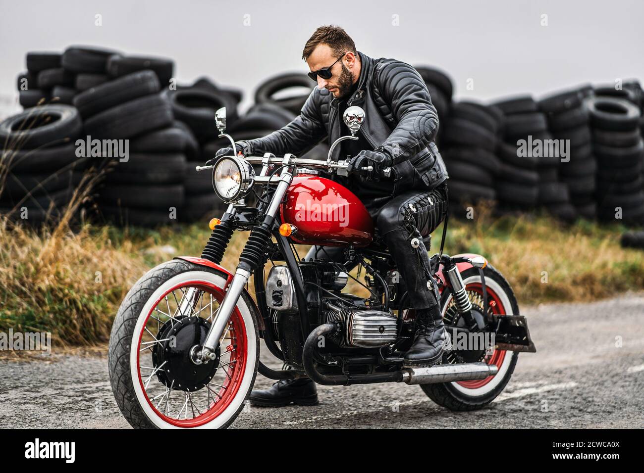 Moto roja con jinete. Un hombre en una chaqueta de cuero negro y pantalones  comienza una motocicleta. Los neumáticos se colocan sobre el fondo  Fotografía de stock - Alamy