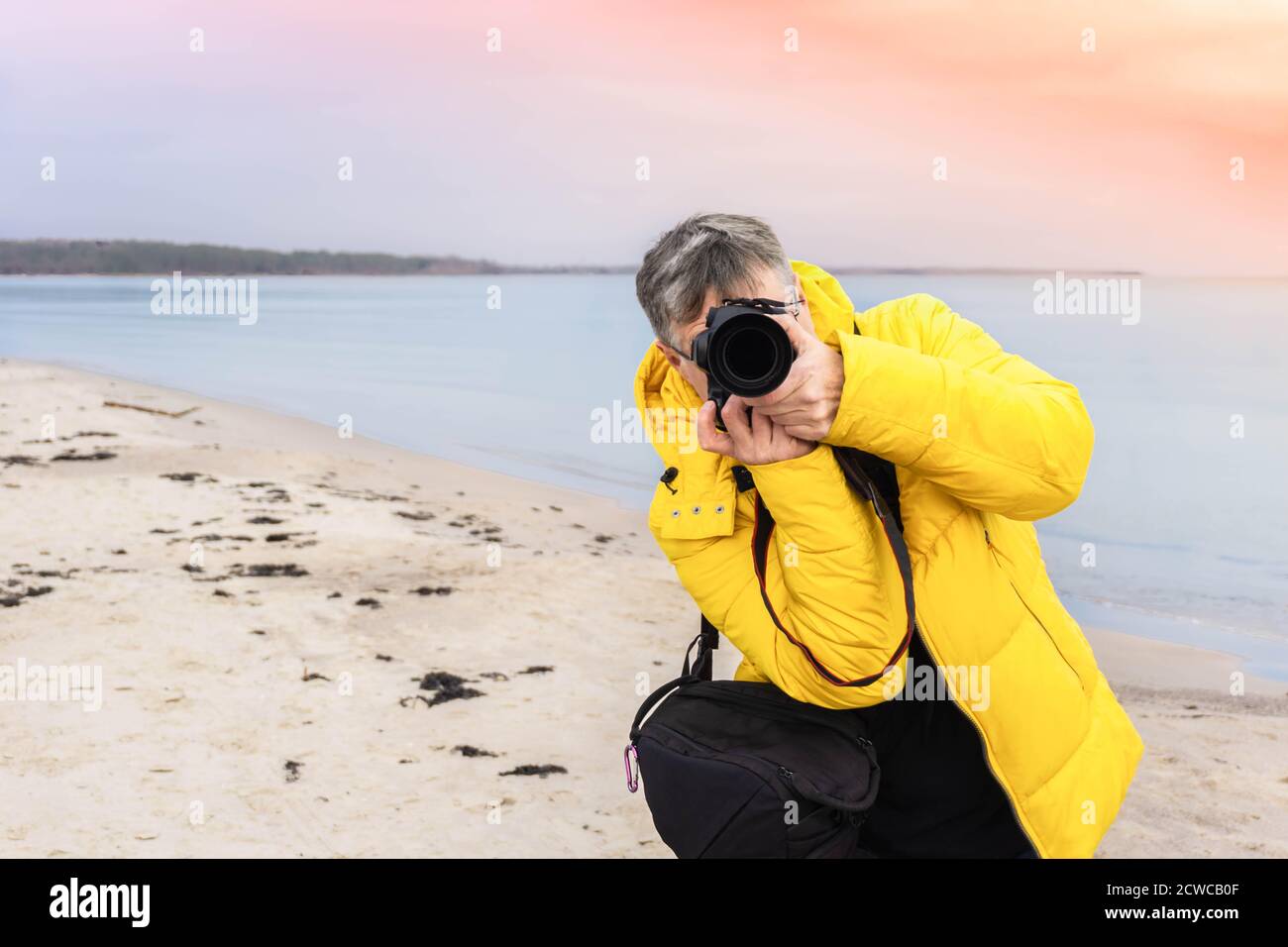 Fotógrafo masculino haciendo fotos en la playa. Fotógrafo viajero en  chaqueta amarilla mirando directamente a través de la cámara en la costa  del mar. Fotografía de viajes Fotografía de stock - Alamy