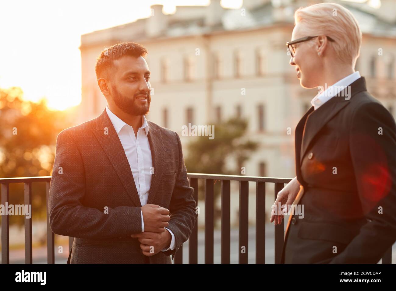 Compañeros de negocios en elegantes trajes negros hablar entre sí estando  de pie en el balcón Fotografía de stock - Alamy
