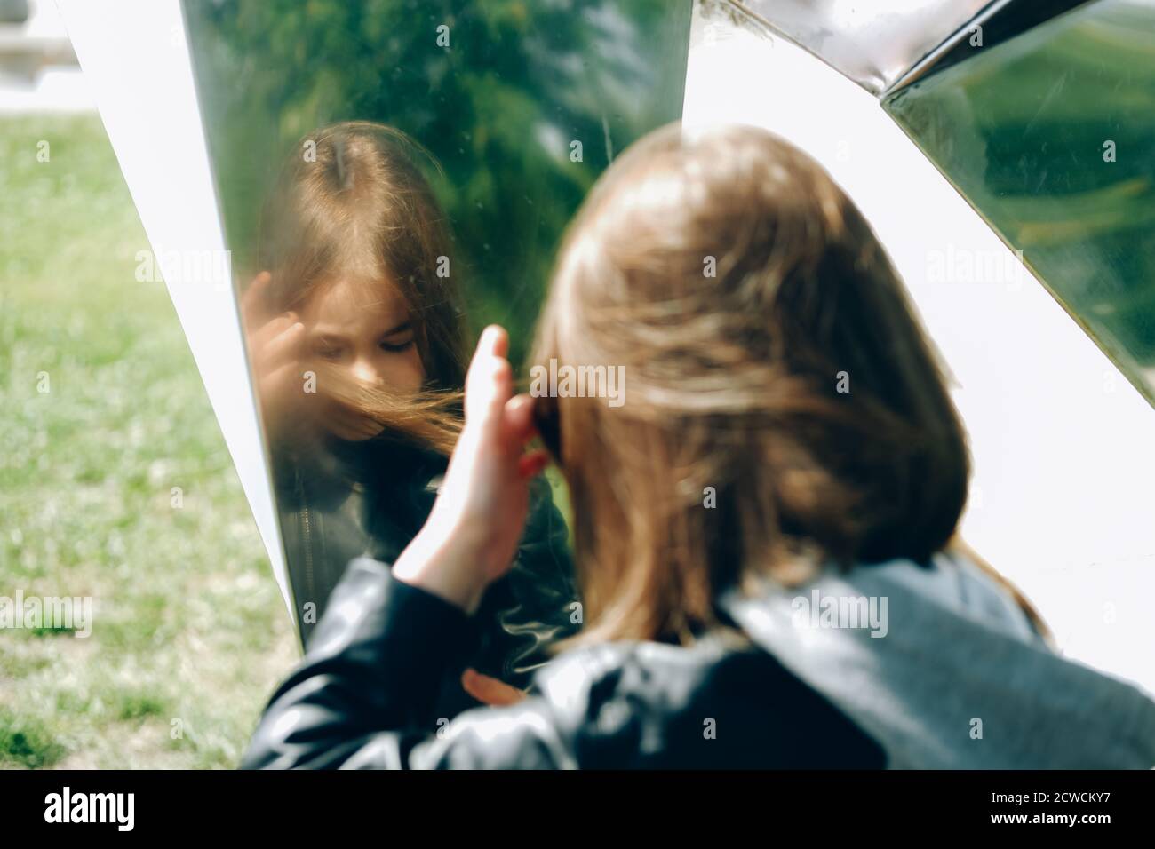 hermosa chica mirando en la superficie del espejo al aire libre doorsona día soleado Foto de stock