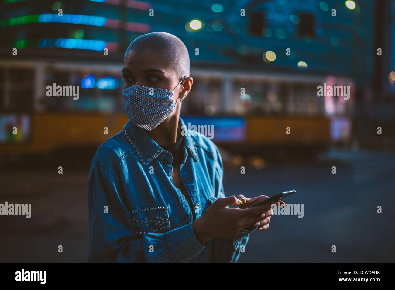 Imagen de una joven que utiliza el teléfono móvil en la calle. Chica con pelo corto caminando por la noche en el centro de la ciudad Foto de stock