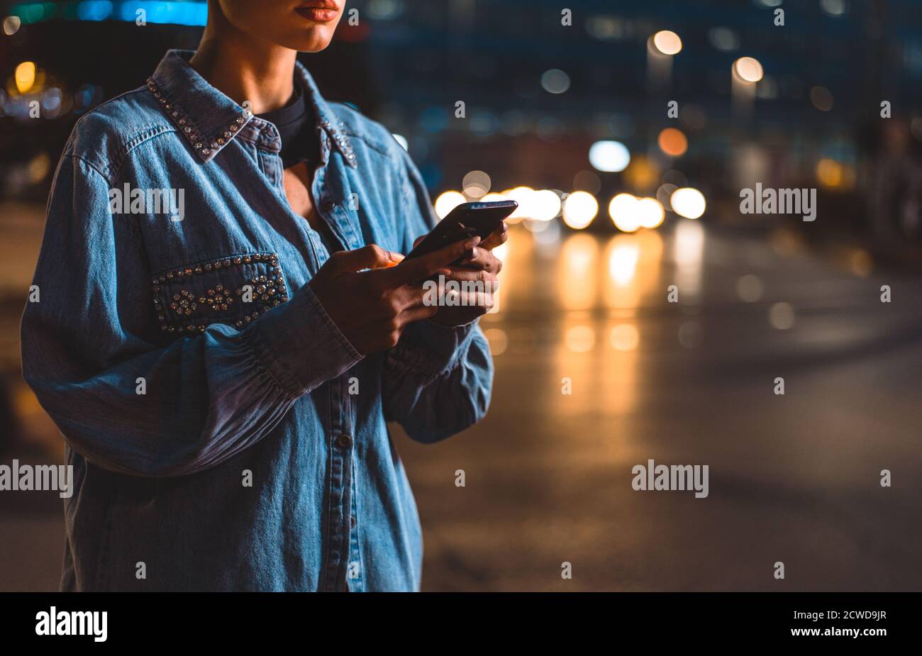 Imagen de una joven que utiliza el teléfono móvil en la calle. Chica con pelo corto caminando por la noche en el centro de la ciudad Foto de stock