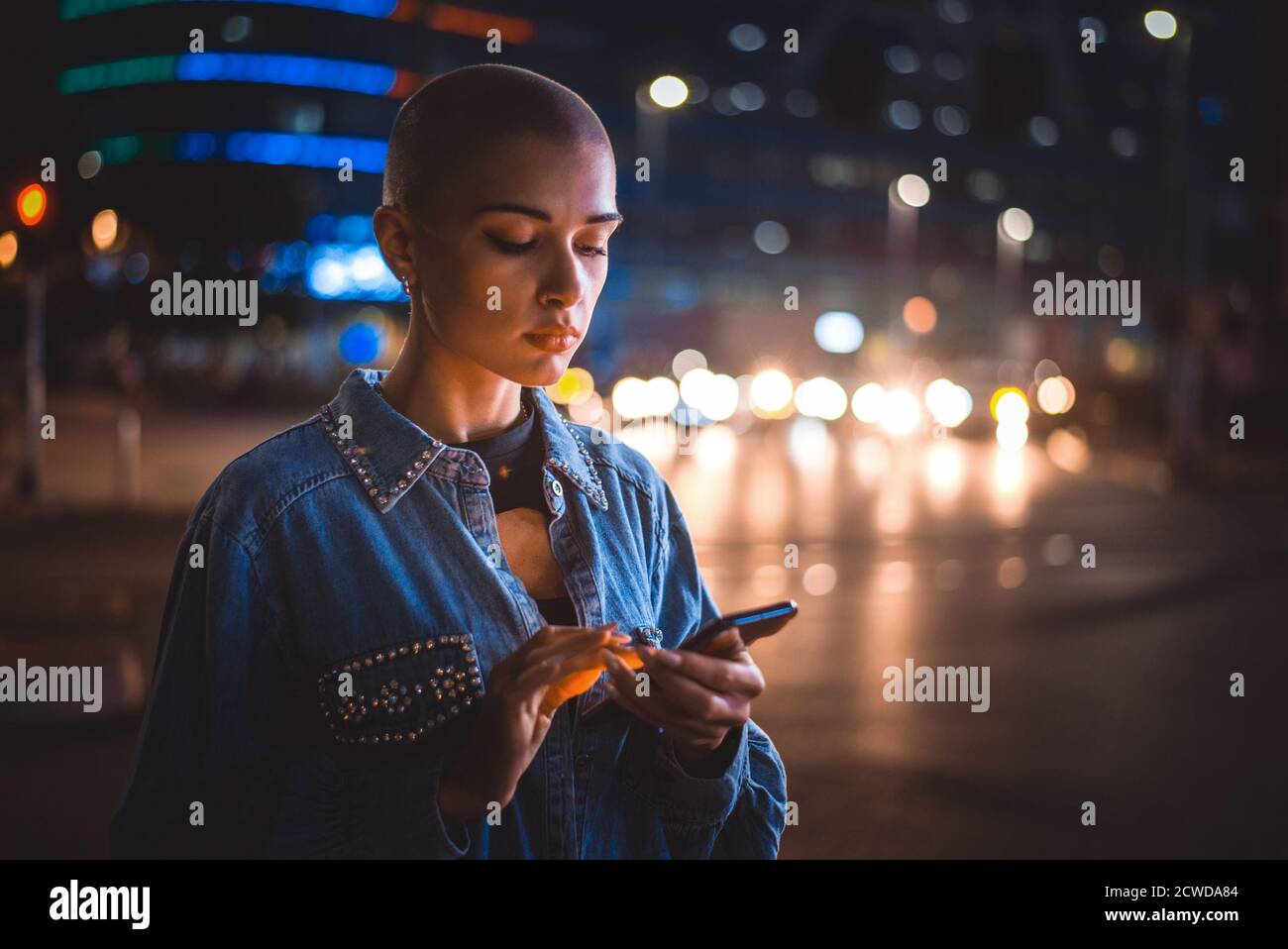 Imagen de una joven que utiliza el teléfono móvil en la calle. Chica con pelo corto caminando por la noche en el centro de la ciudad Foto de stock