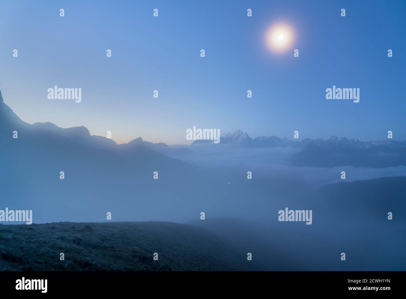 Luna llena en el foggy cielo sobre Marmolada al atardecer, Dolomitas, Trentino, Italia Foto de stock