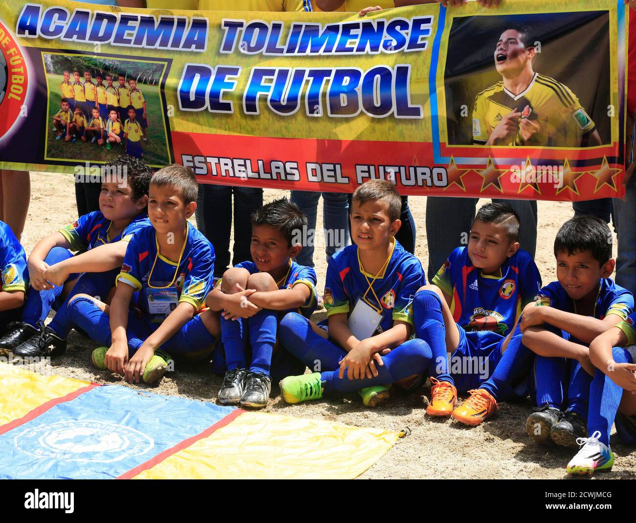 Young soccer players pose with a banner of their soccer school name before a practice session in a field where Colombia's player James Rodriguez played in Ibague July 2, 2014. Colombian youth coach Armando Yull Brenner never suspected he had found one of the world's greatest talents as he saw seven-year-old James Rodriguez dribble past teammates to score almost two decades ago on a shabby neighborhood pitch. James, whose baby-face is instantly recognizable in the photos lining Brenner's office, is perhaps the biggest break-out star at this World Cup. He and his teammates have whipped Colombia Foto de stock