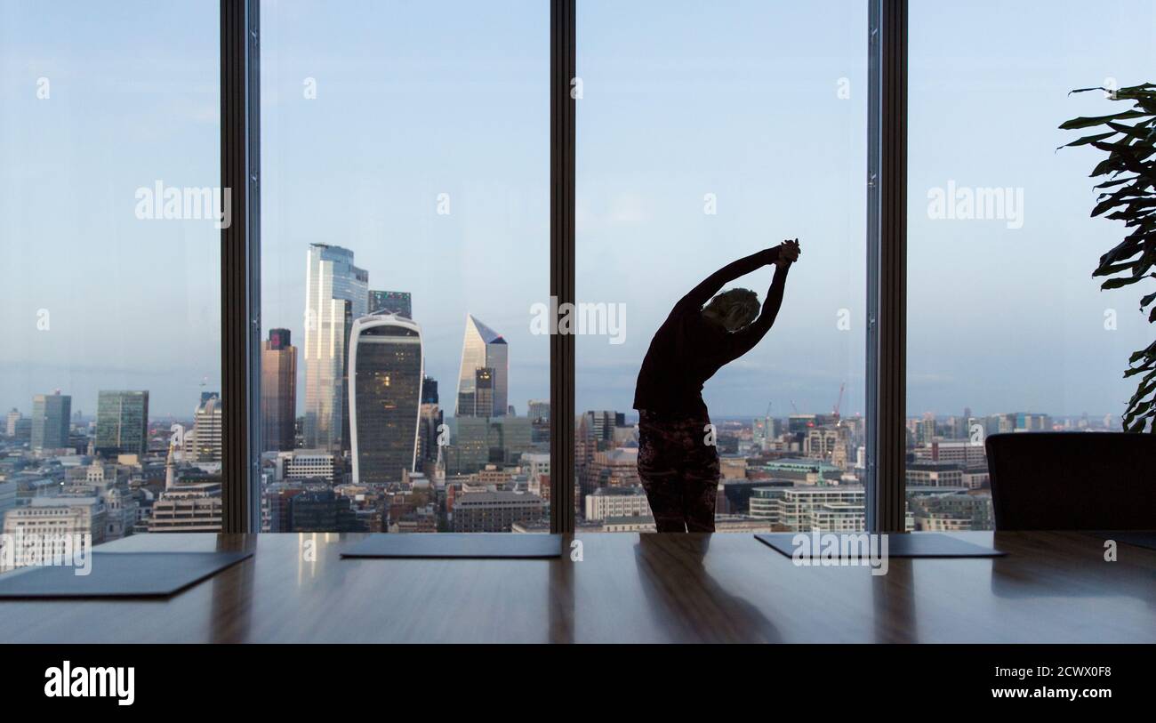 Mujer de negocios estirándose en una ventana de oficina de gran altura, Londres, Reino Unido Foto de stock
