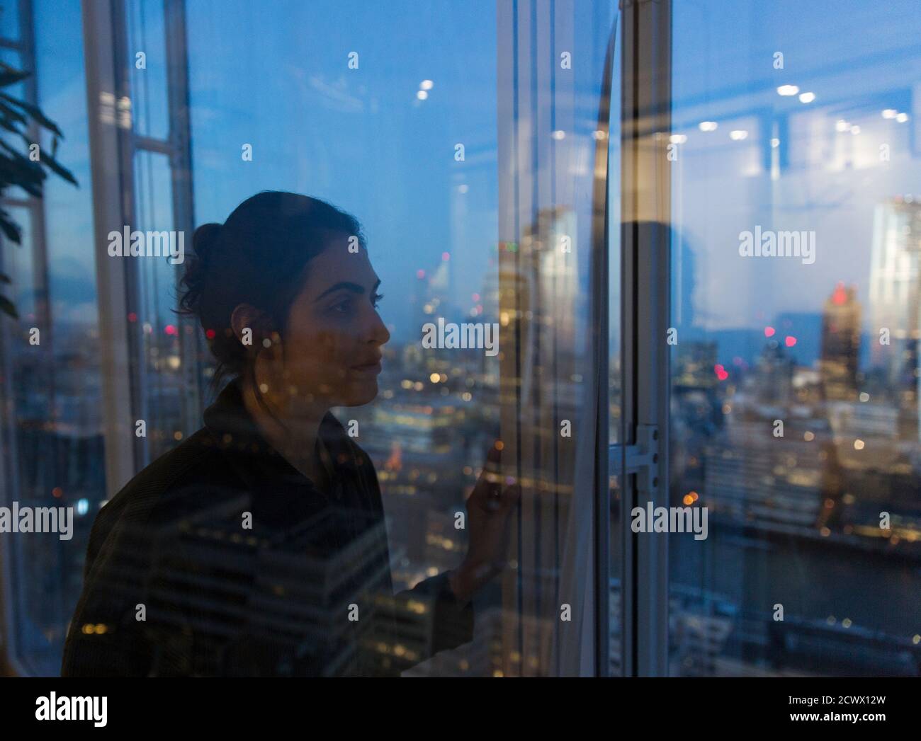 Una mujer de negocios pensativa trabajando tarde en una ventana de oficina de gran altura Foto de stock