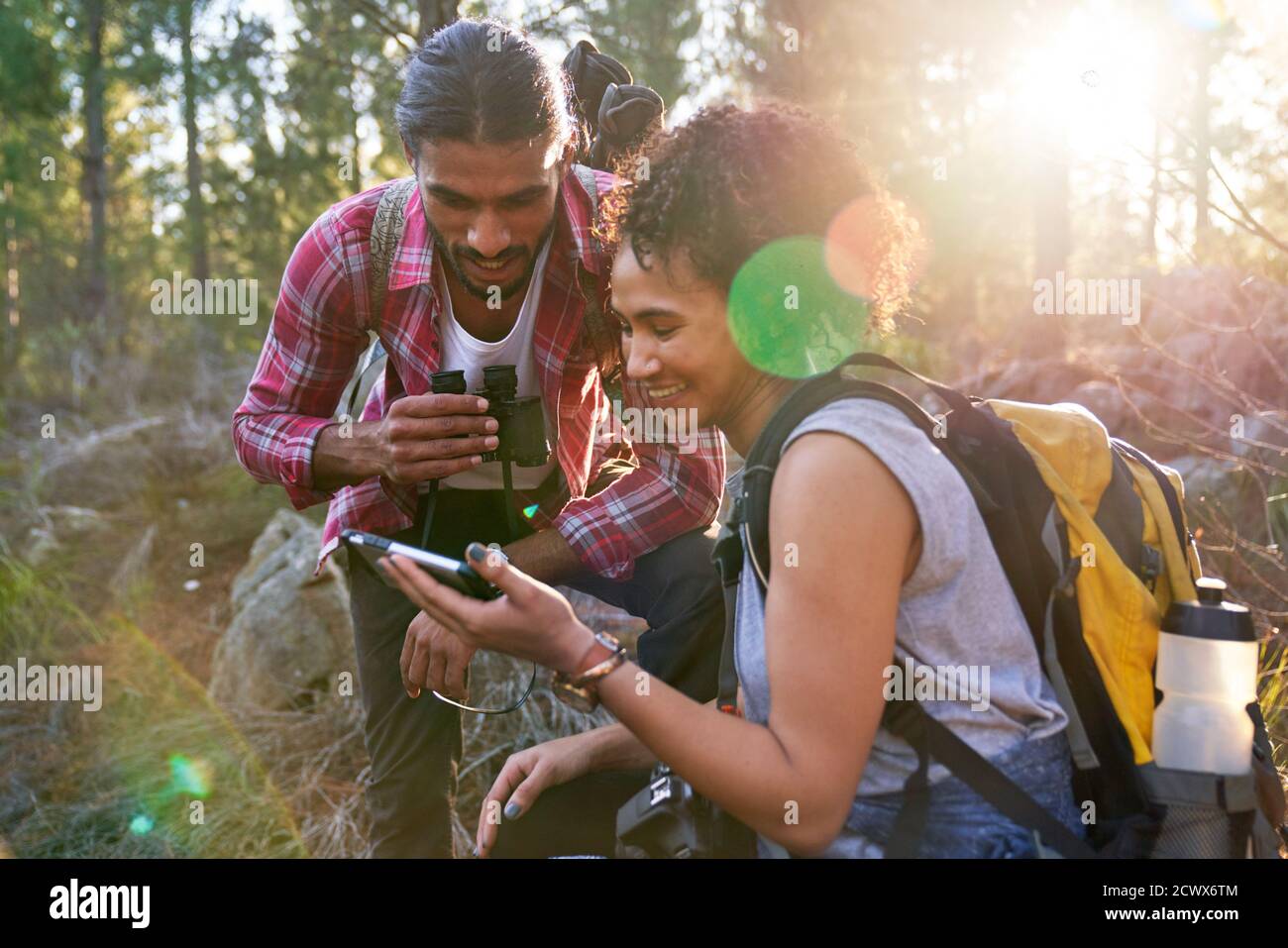 Feliz joven pareja de senderismo utilizando el teléfono inteligente en bosques soleados Foto de stock