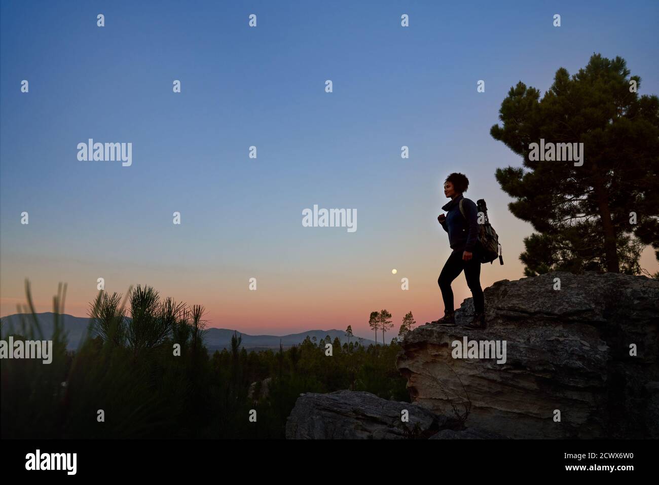 Joven mujer hiker en roca en el desierto tranquilo escénico en atardecer Foto de stock