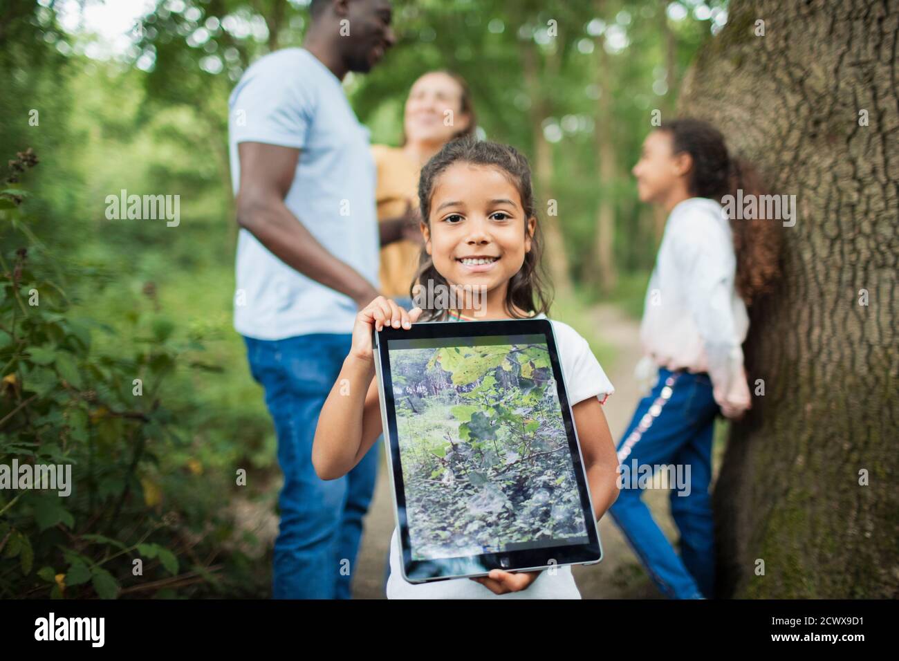 Retrato niña sosteniendo tableta digital con fotografía de planta en bosques Foto de stock