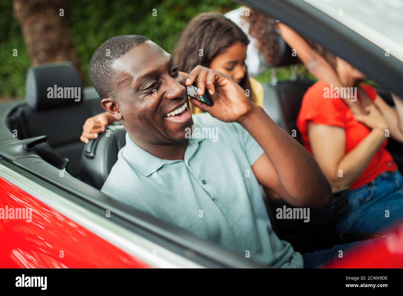 Hombre feliz hablando en el teléfono inteligente en convertible con la familia Foto de stock