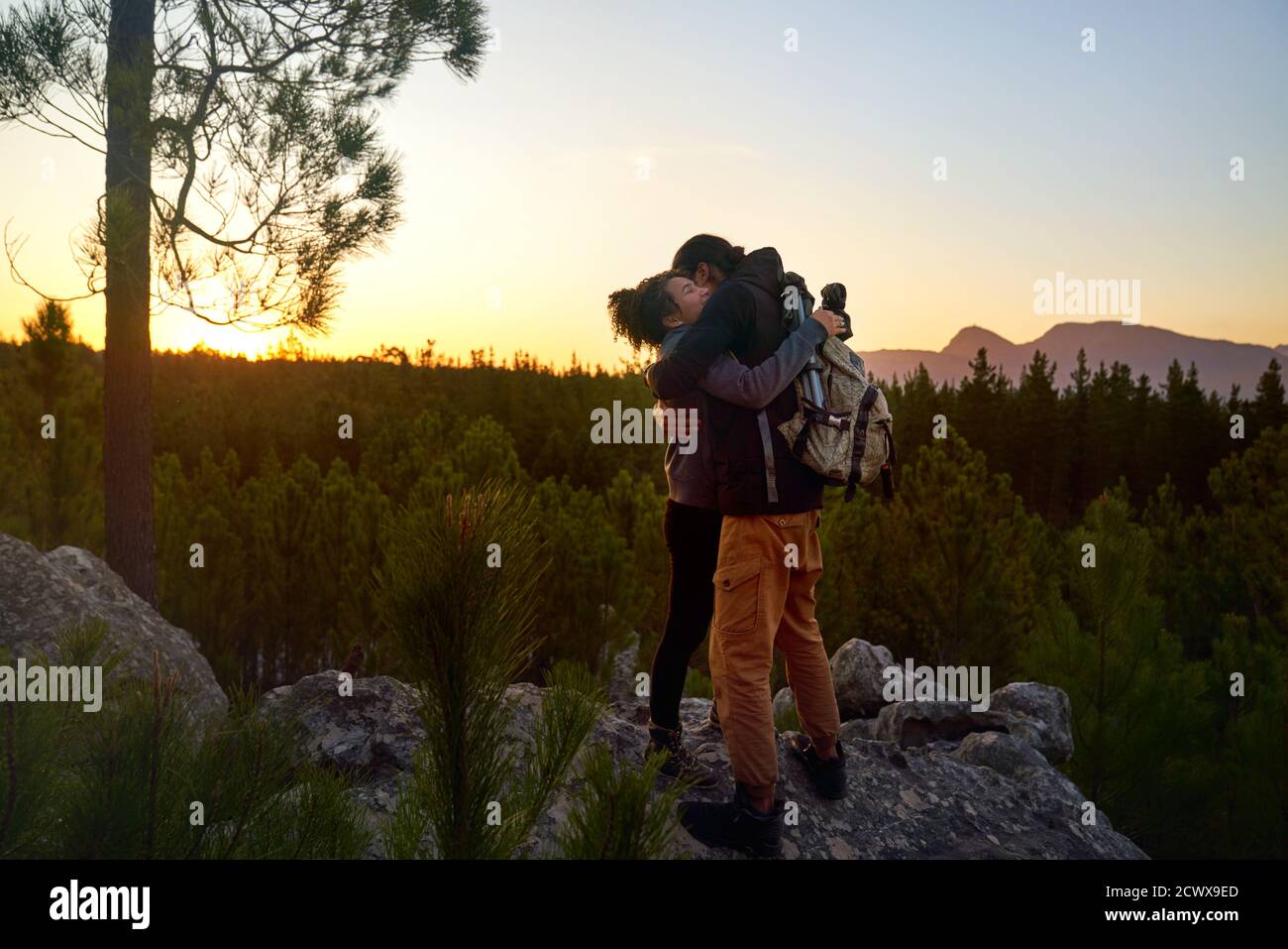 Cariñoso joven pareja de excursionistas caminando en roca en bosques de puesta de sol Foto de stock