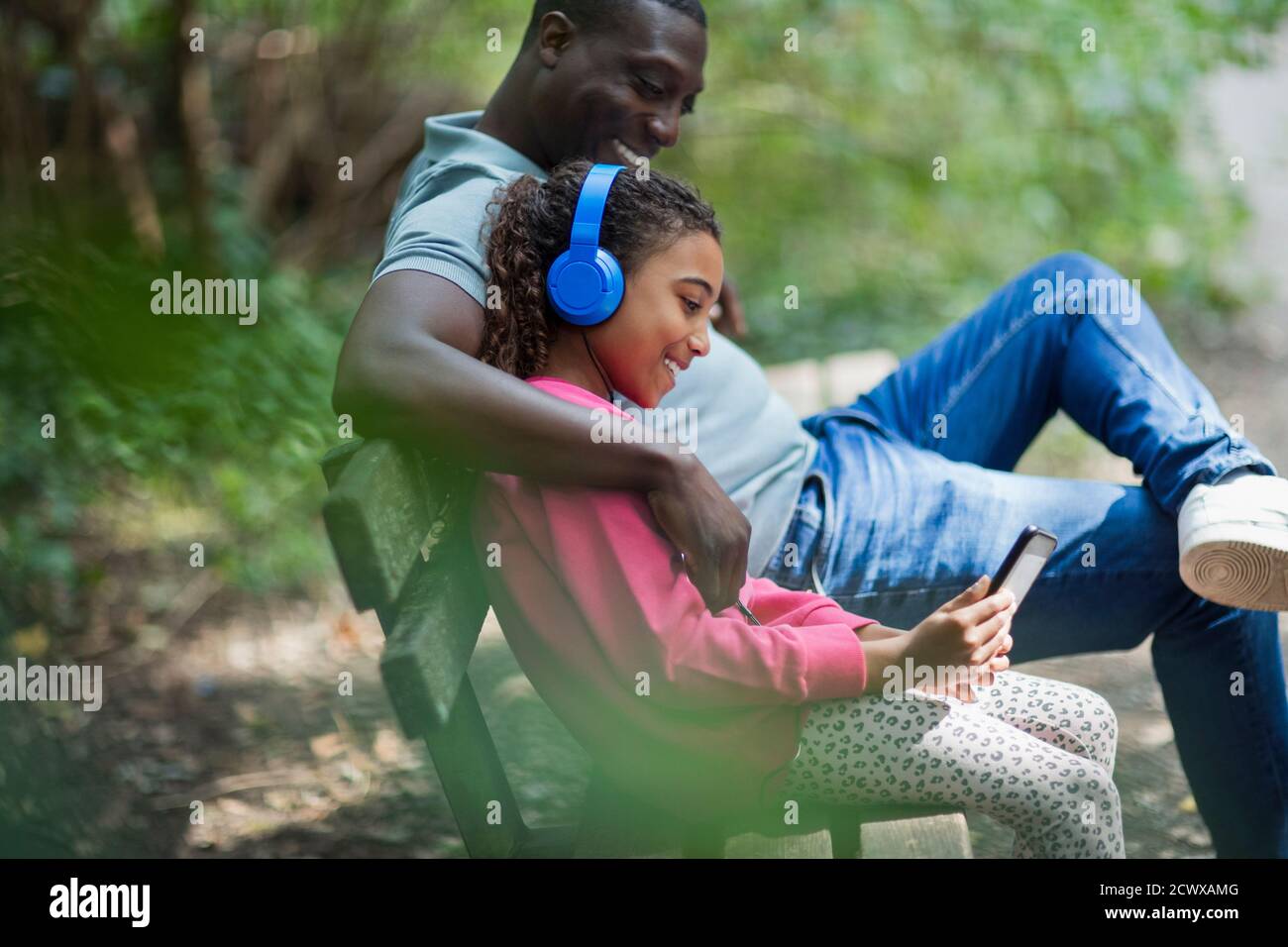 Padre e hija con auriculares y tableta digital en el parque banco Foto de stock