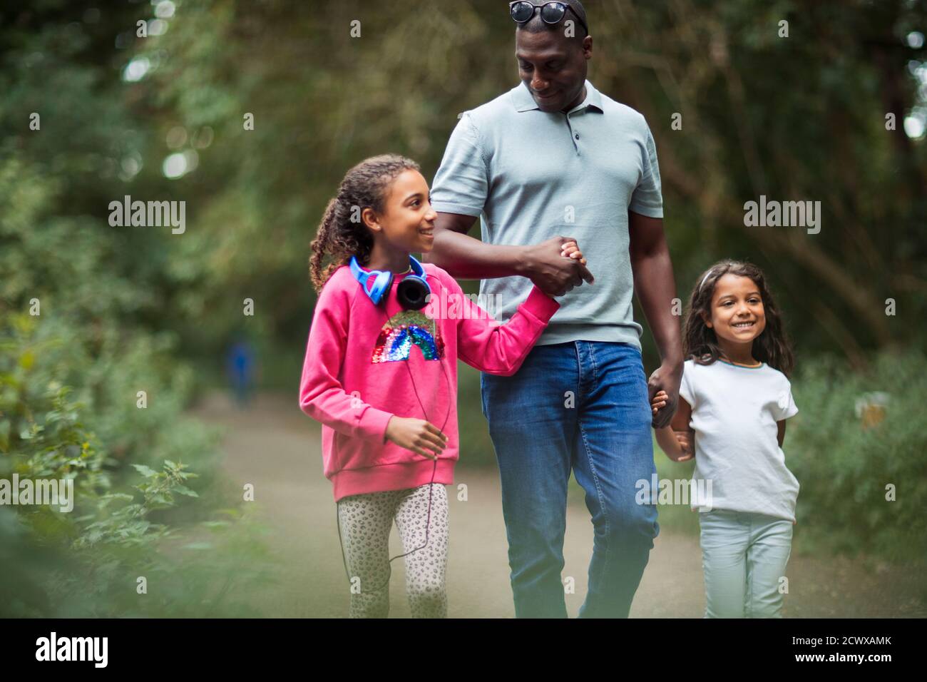 Feliz padre e hijas con las manos caminando por el camino del parque Foto de stock