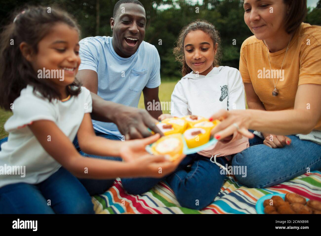 Familia disfrutando de pastelitos en la manta de picnic en el parque Foto de stock